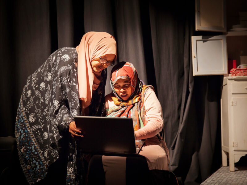 Two women wearing hijabs use a laptop together
