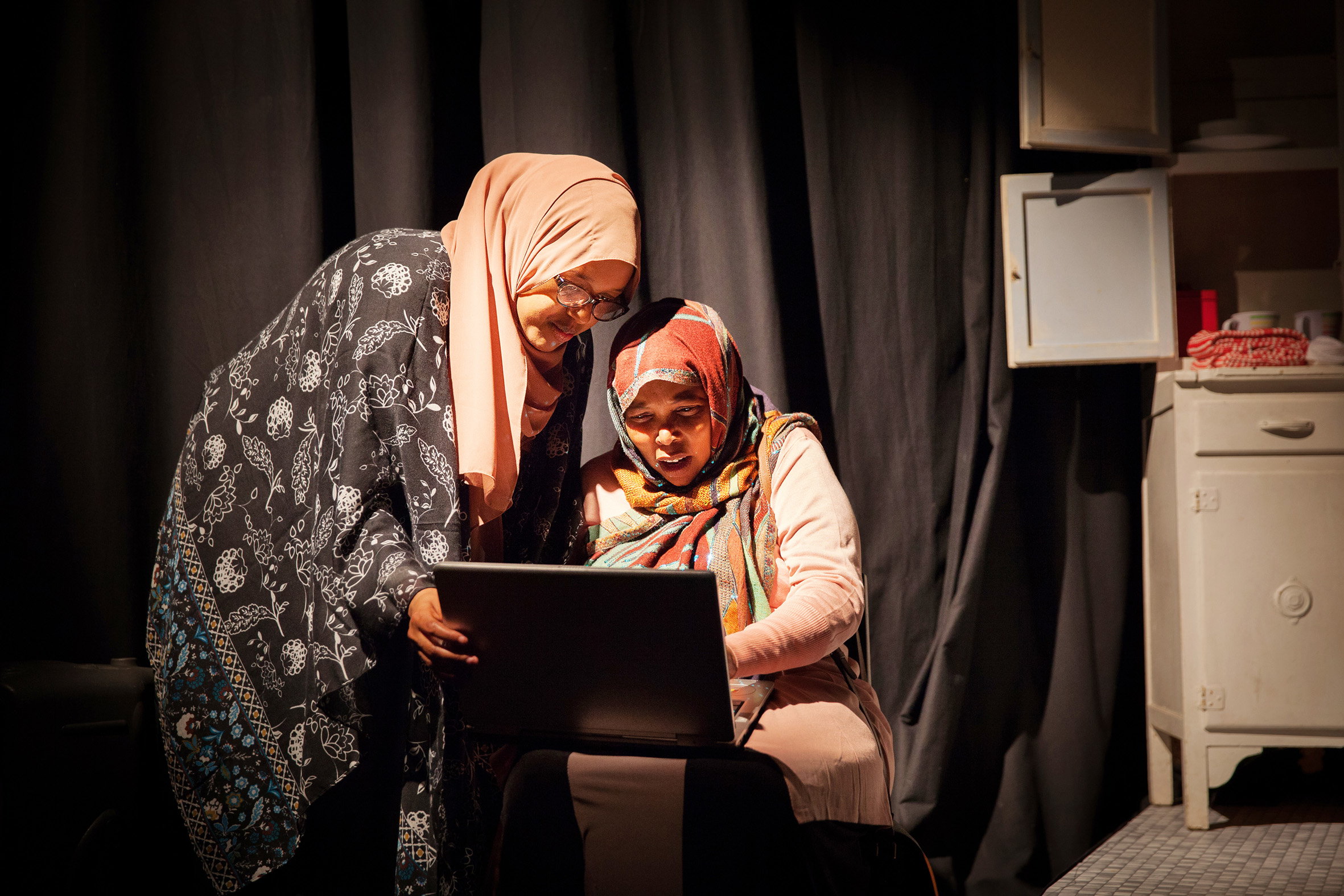 Two women wearing hijabs use a laptop together