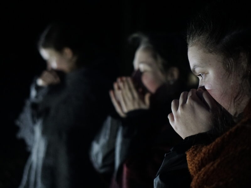 Three young actors in the dark, hold their faces as though in fear