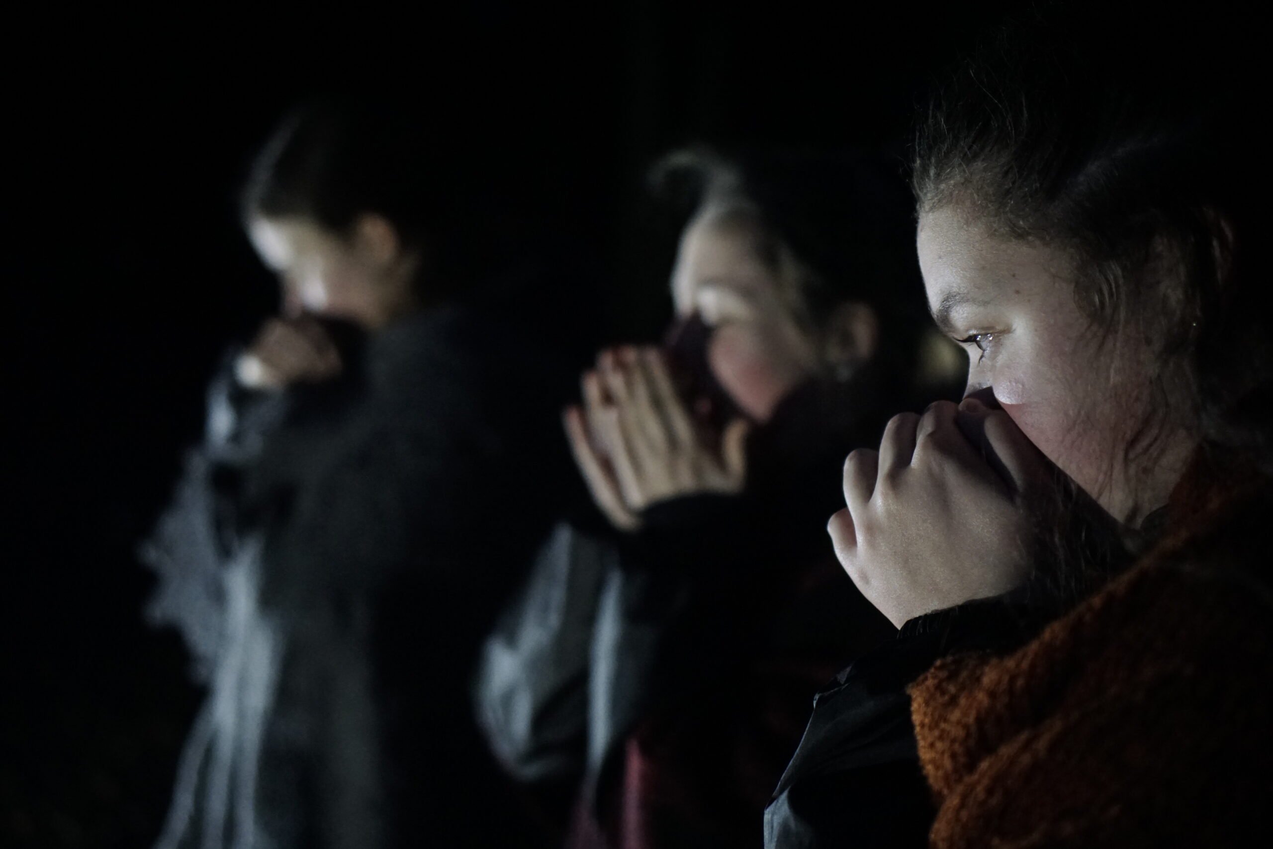 Three young actors in the dark, hold their faces as though in fear