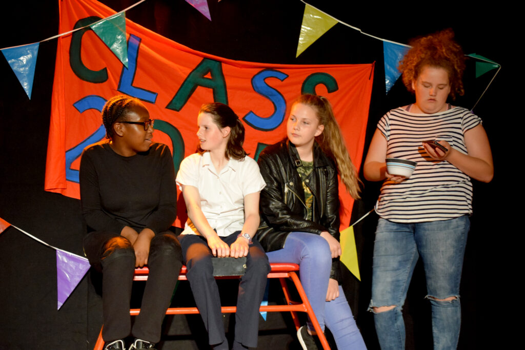 Four young actors sit in front of a banner that appears to say “Class 2015”