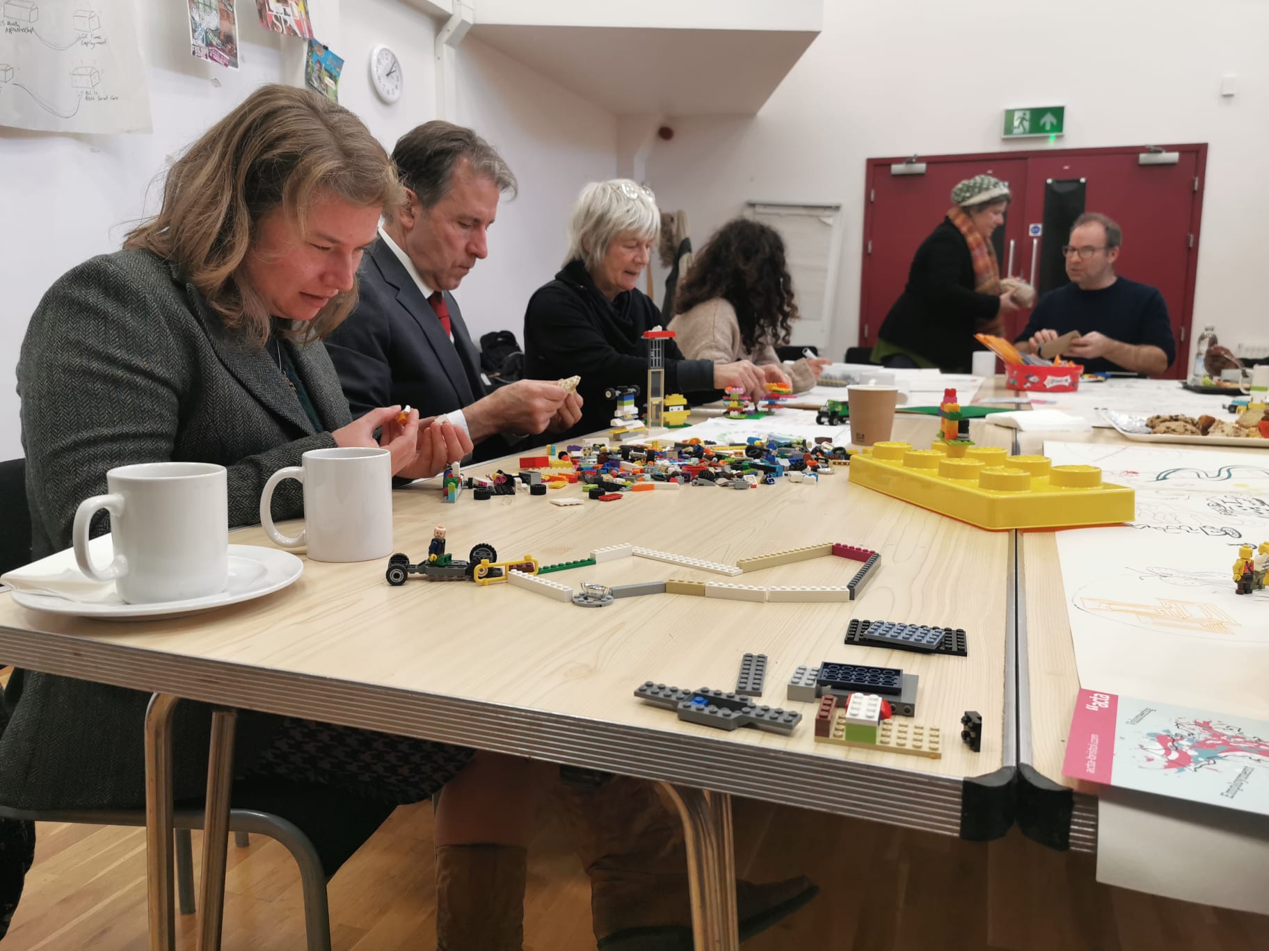 Five people sit at a big table, using lego bricks to help communicate their ideas