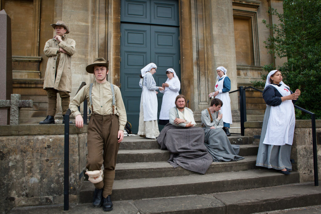 Actors dressed as WW1 injured soldiers and WW1 nurses, sit and stand on the steps of an old Crypt
