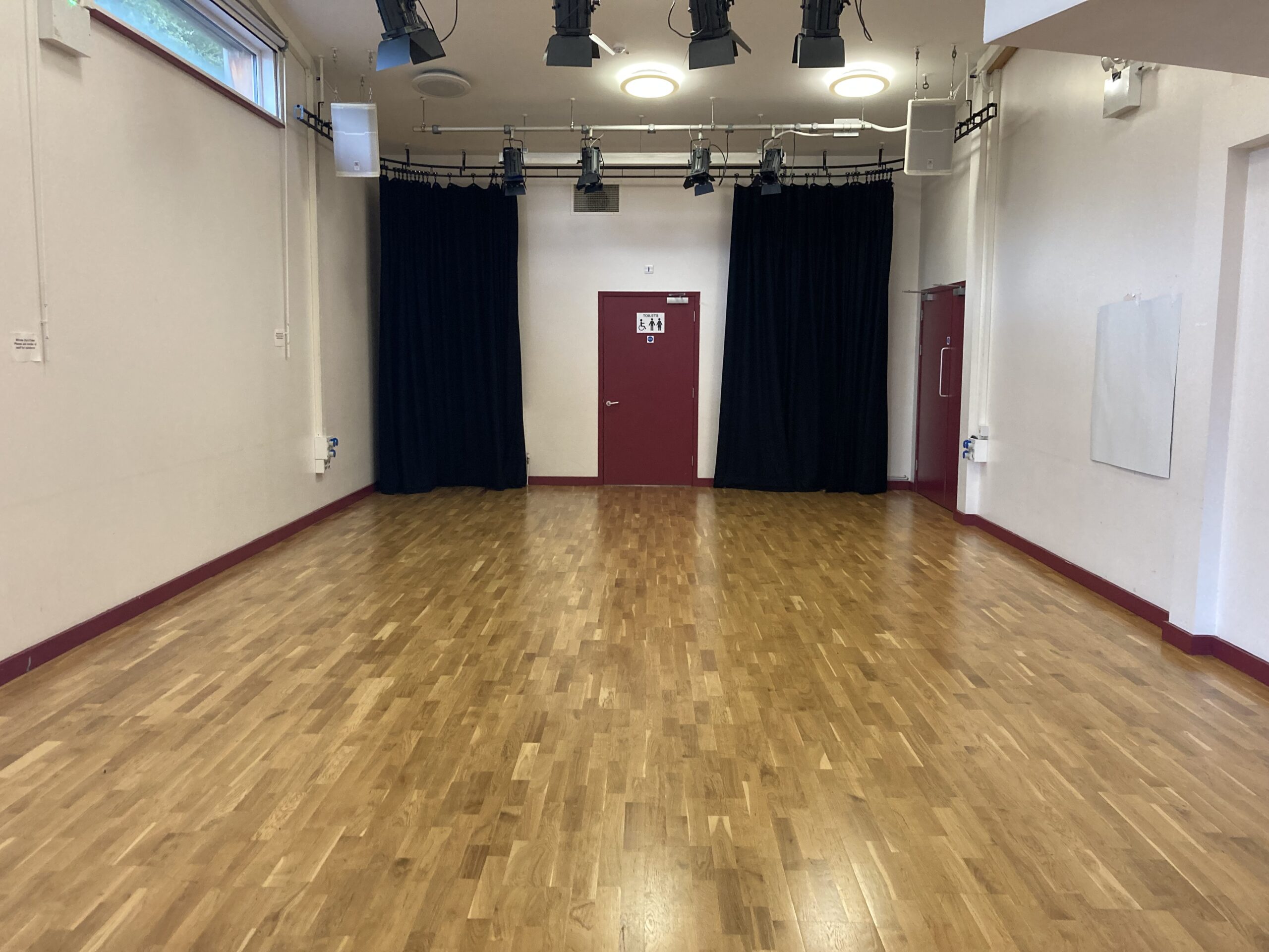 An empty studio room - the floor is wood and the walls are white