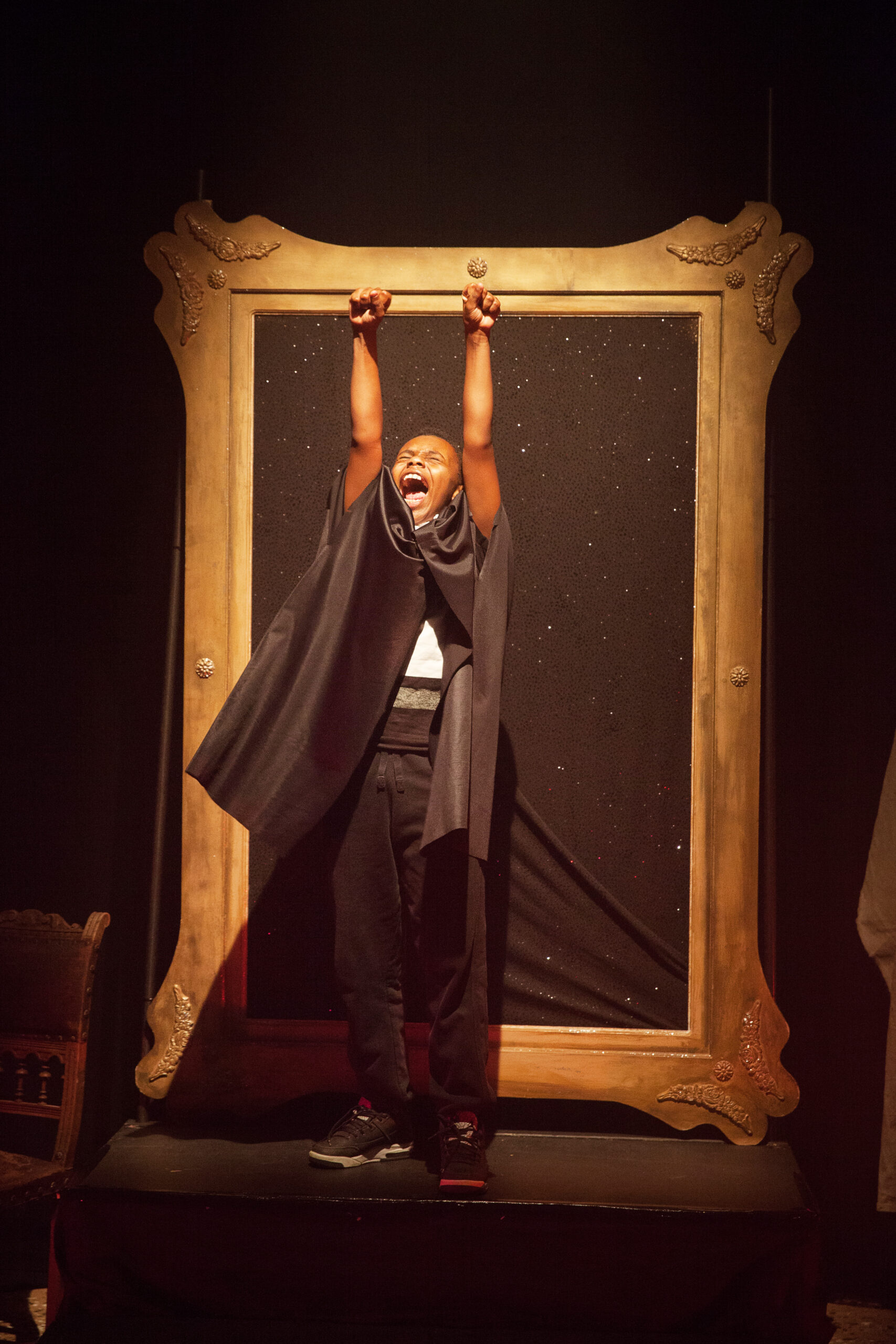 An actor reaching up to the sky in front of a large wooden frame