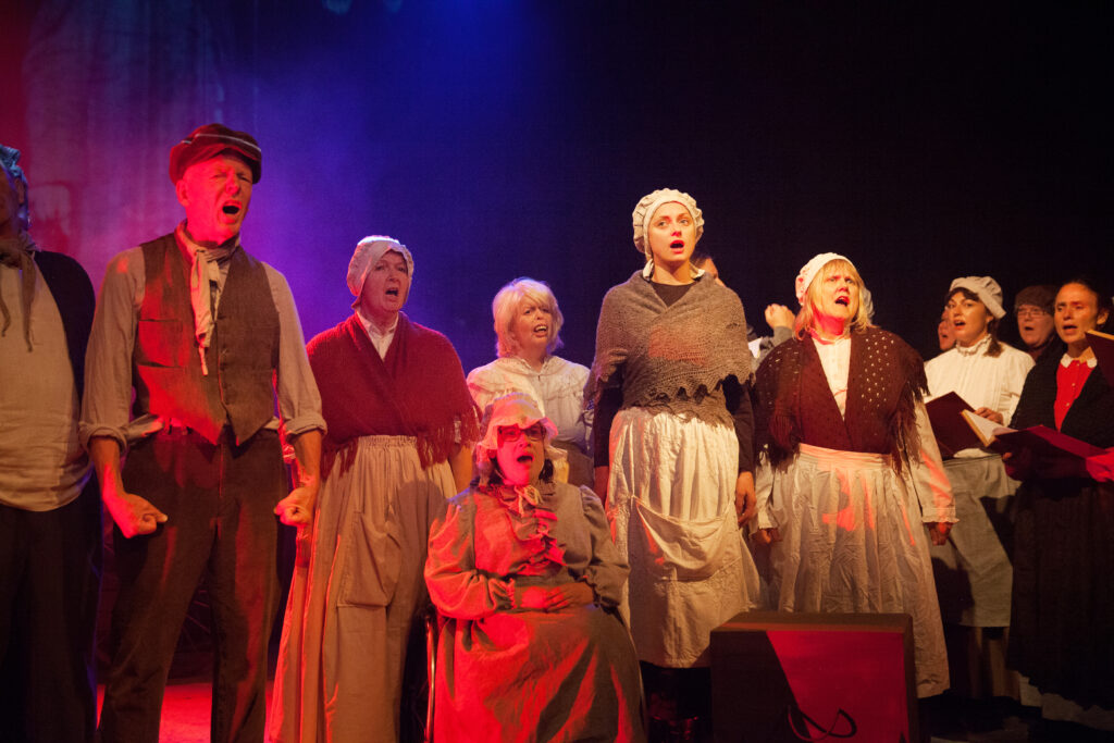 Six actors on stage wearing 1800s style clothing and singing all together